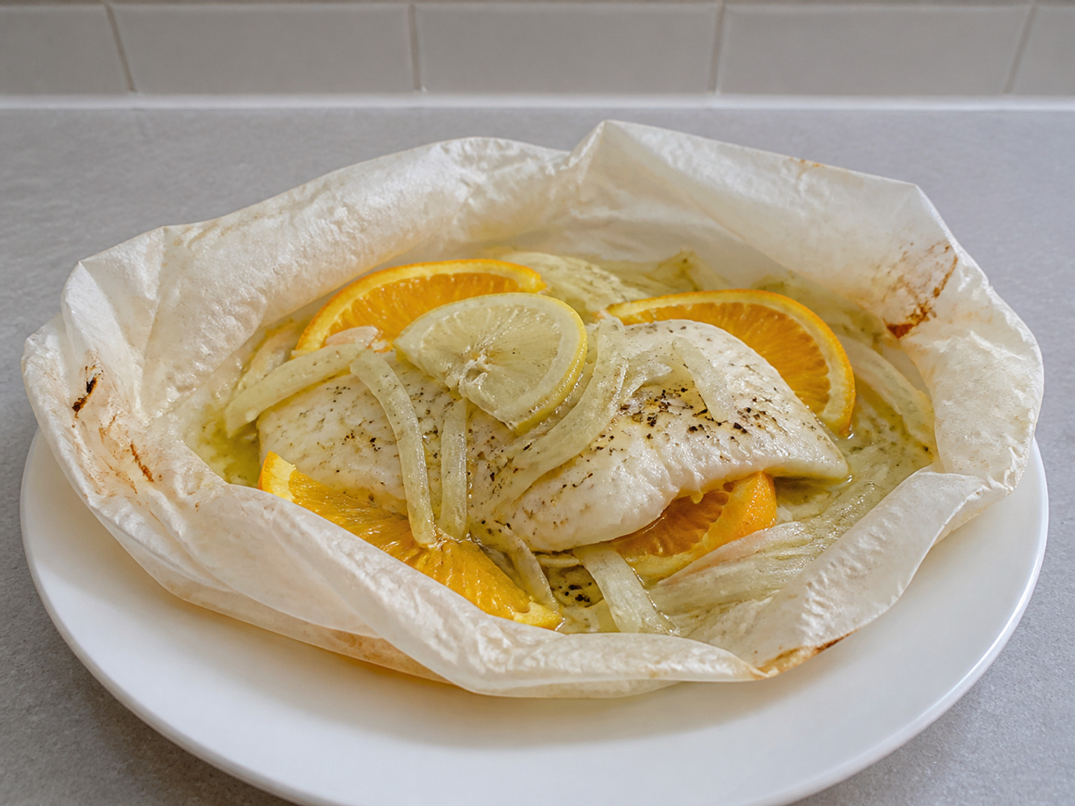 Fillet Ikan Papillote dengan Adas dan Jeruk: Empat bungkusan kertas mengukus ikan putih bersama irisan adas dan jeruk, sehingga tiap porsi tetap lembap dan harum tanpa saus berat.