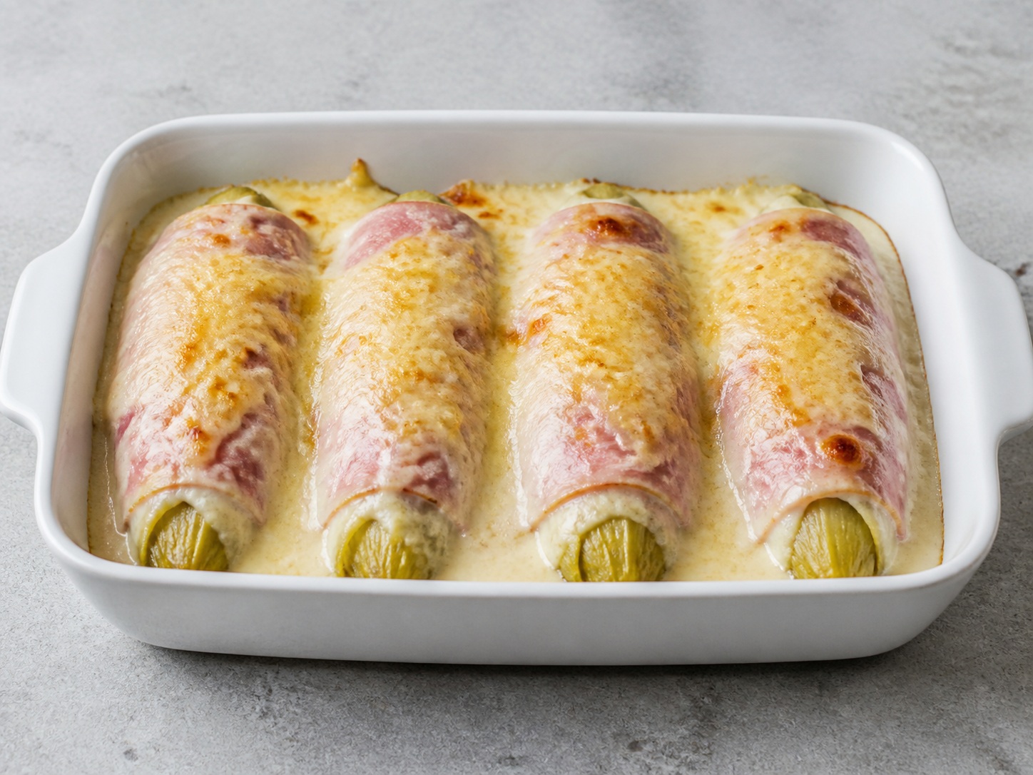 Gratin Endive dan Ham Prancis: Endive empuk dibungkus ham satu per satu, disiram saus putih ringan, lalu dipanggang dengan keju keemasan.