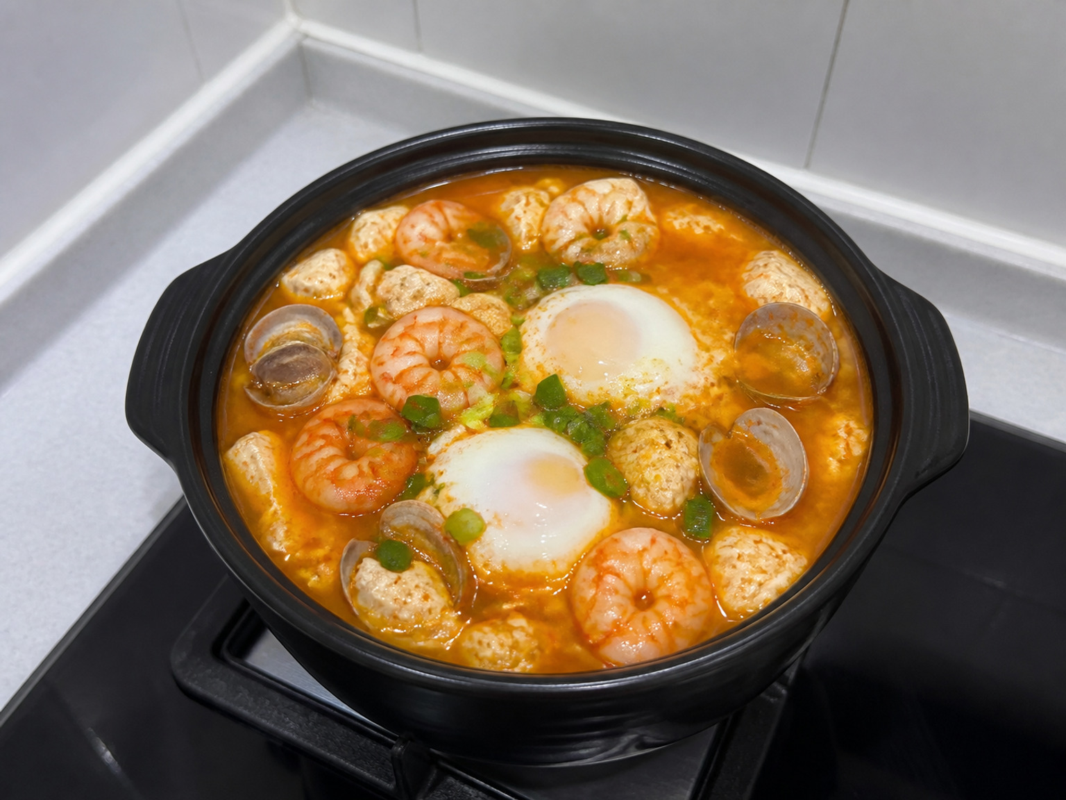 Korean Seafood Soft Tofu Stew: Clear anchovy broth, red chilli oil, spoon-soft tofu, clams, prawns and eggs simmer together in one bubbling pot.