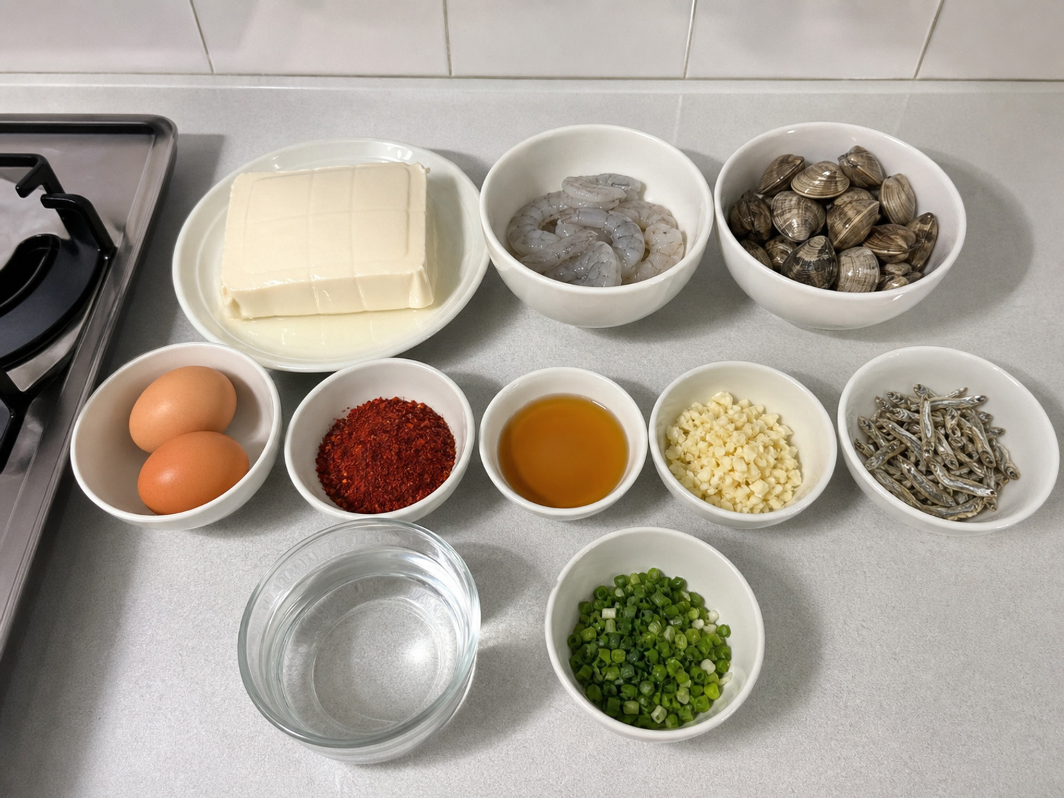韓式海鮮嫩豆腐鍋: 600 克 滑豆腐, 180 克 蝦, 250 克 新鮮蜆, 2 個 雞蛋, 2 湯匙 韓式辣椒粉, 1 湯匙 麻油, 3 瓣 蒜頭, 20 克 江魚仔, 900 毫升 清水, 2 條 蔥